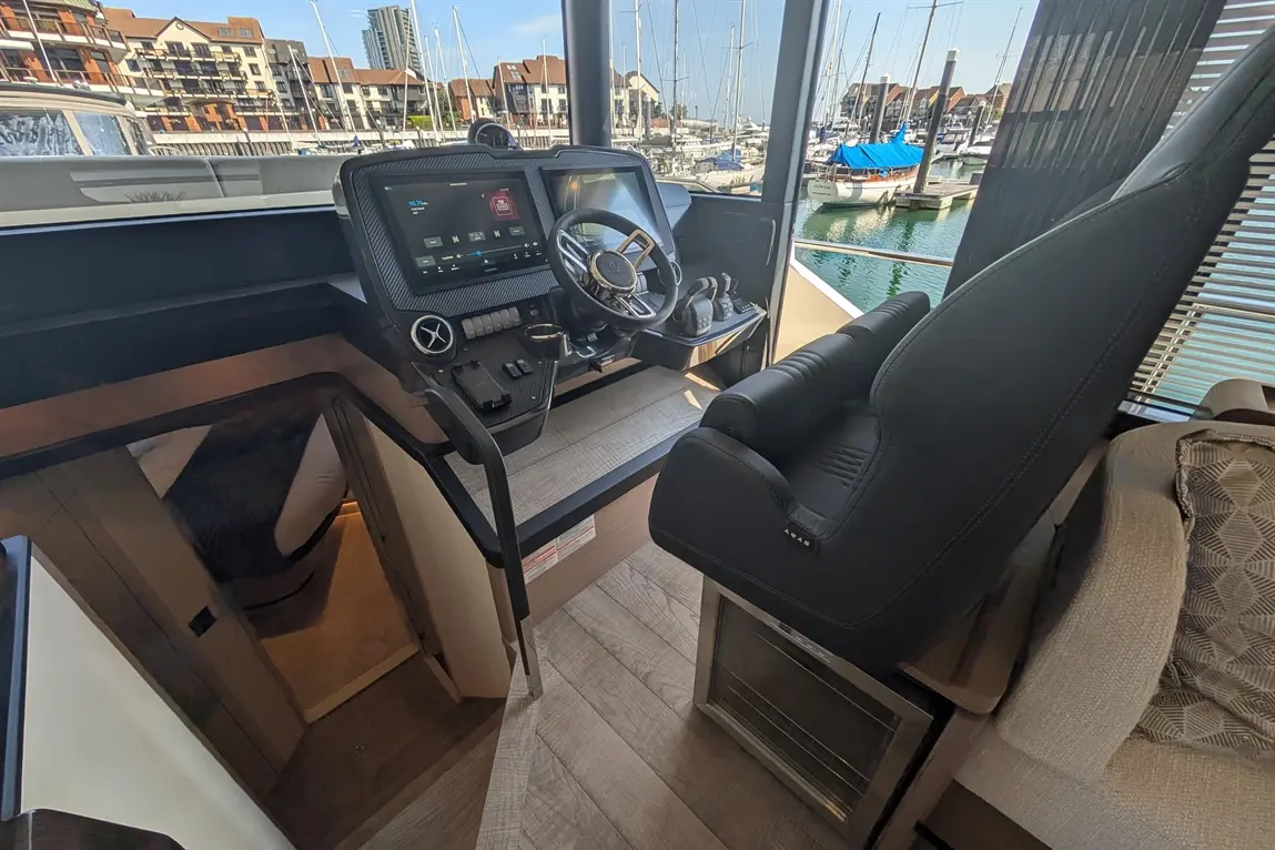 Interior view of a modern boat's cockpit, featuring a sleek control panel, steering wheel, and comfortable seating by the marina.